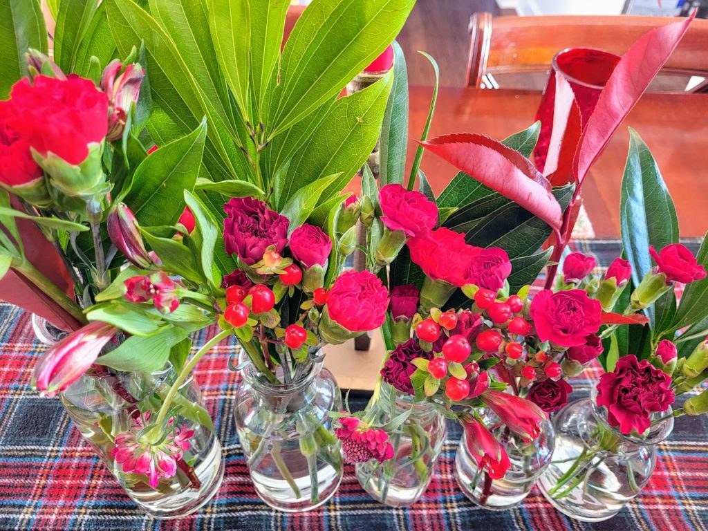 five small flower arrangements showing red flowers, berries and green leaves