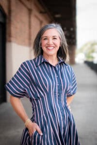 A photo of the author, in a blue striped dress. She is smiling and happy.